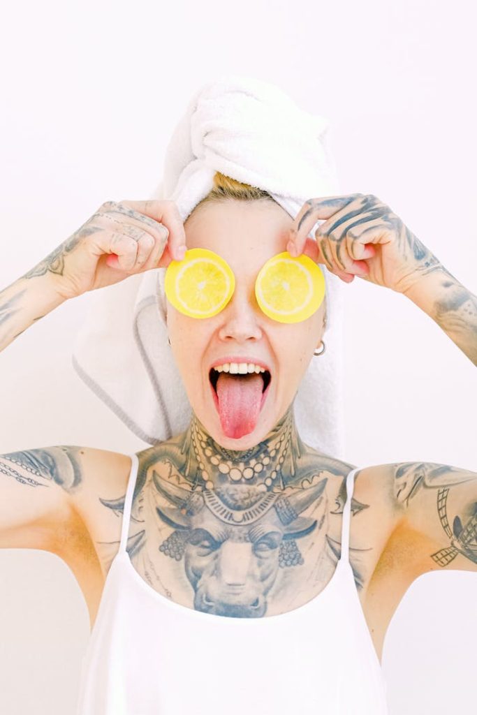 Fun portrait of a tattooed woman with towel turban, playfully holding lemon slices and sticking out her tongue.