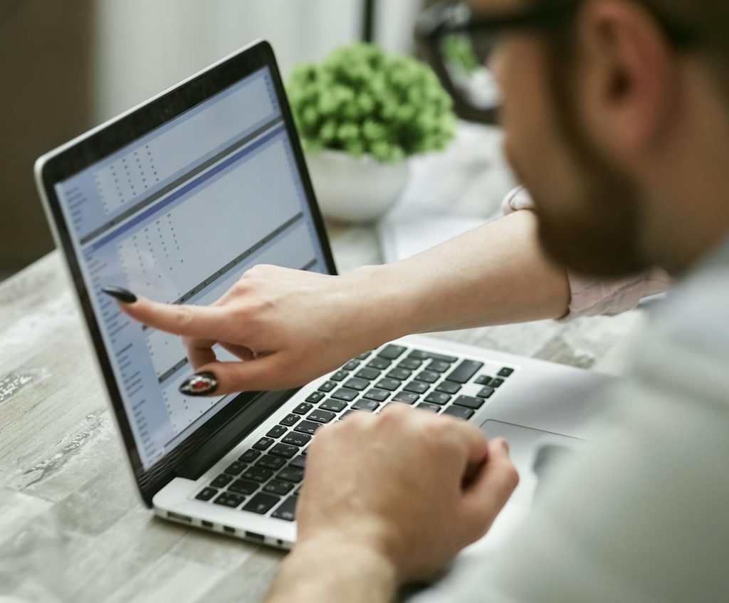 Two people working on a laptop analyzing data, pointing at screen.